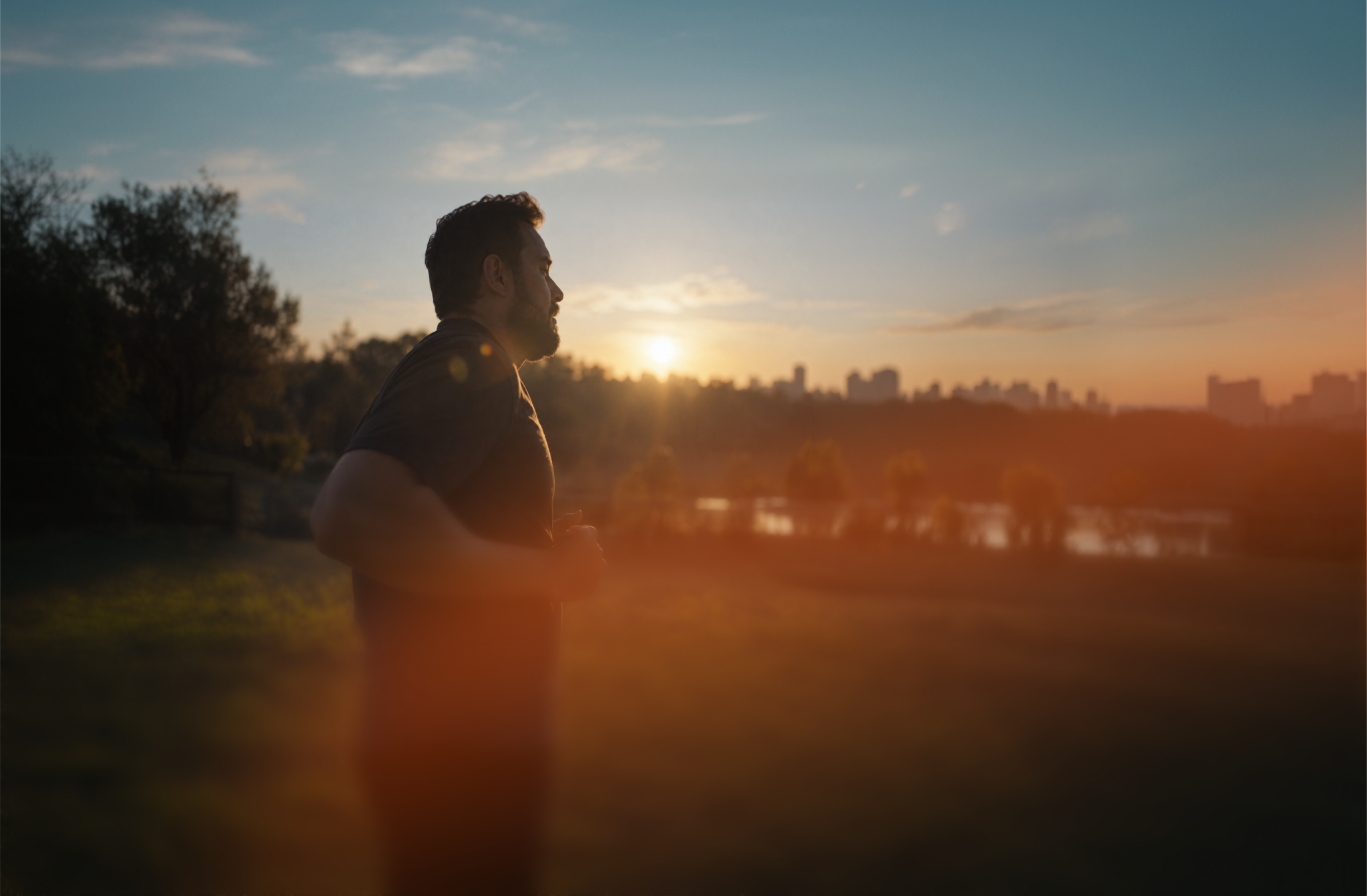 A man running at sunset with a city skyline in the distance